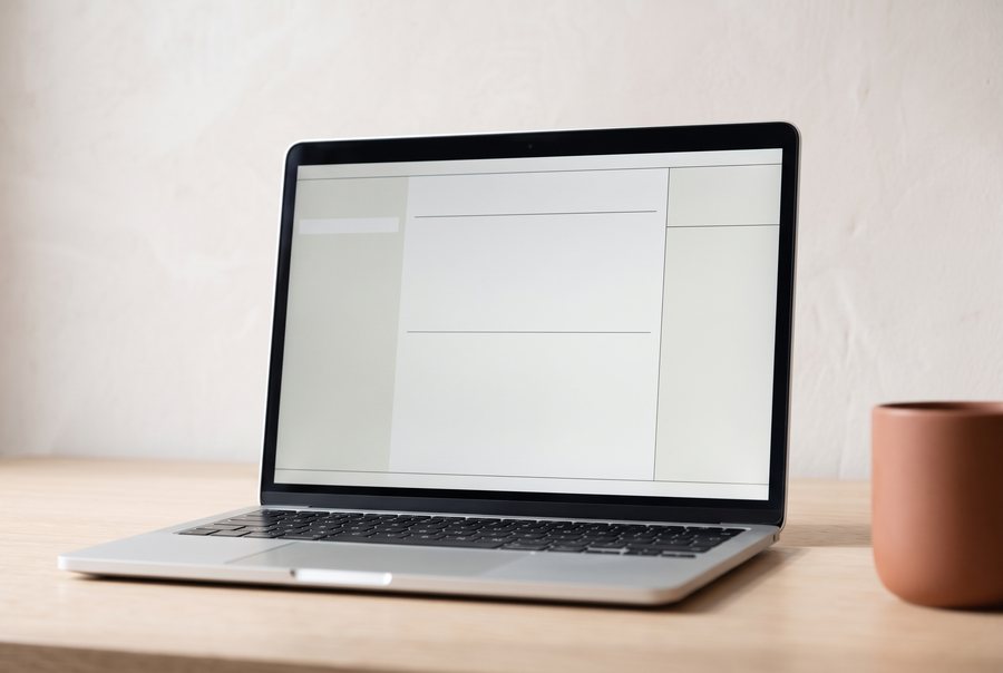 Close view of the open laptop on the pale oak desk, its screen calm and orderly, the terracotta mug soft behind it.